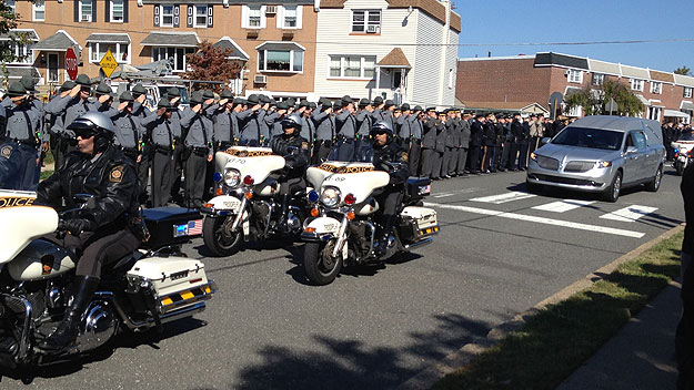 (A line of police officers salute as the hearse carrying the body of Pa. state trooper David Kedra, accompanied by a motorcycle escort, passes by.  Photo by Kim Glovas)